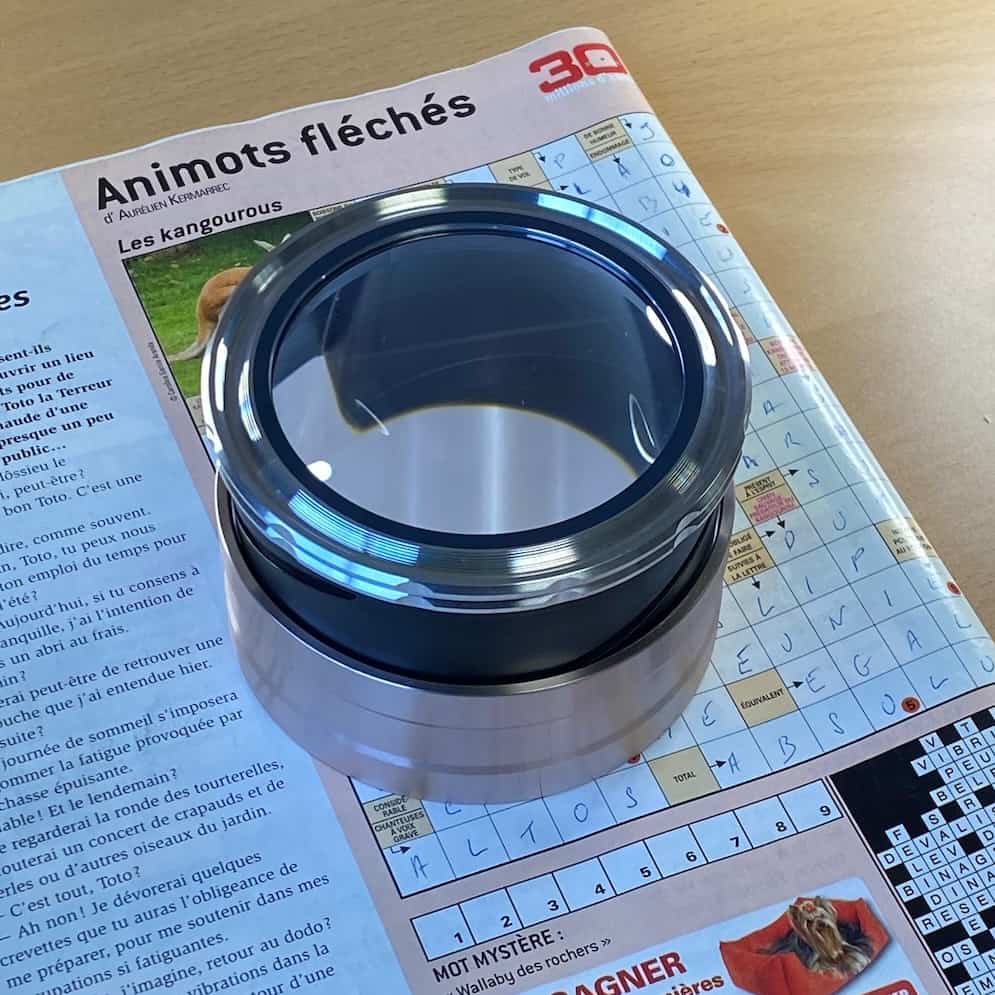 Loupe dôme éclairante rechargeable utilisée sur des mots croisés par une personne malvoyante